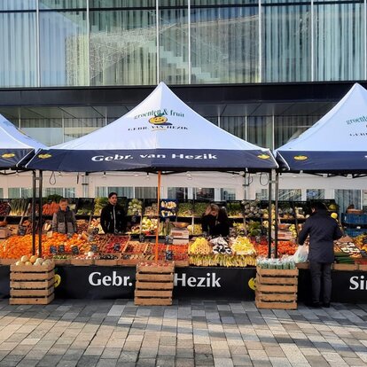 Three connected foldable market gazebos with fruit sellers and a large selection of fresh fruit.