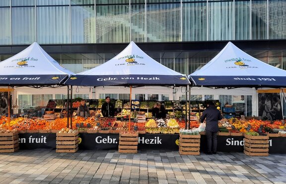 Drei verbundene faltbare Marktzelte mit Obstverkäufern und einer großen Auswahl an frischem Obst.