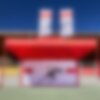 Roter Faltpavillon mit einer bedruckten Seitenwand und roter Struktur. Der Faltpavillon steht im Stadion, dahinter sieht man die Ränge.