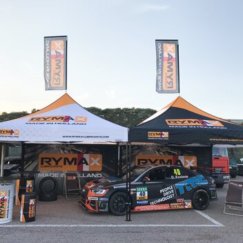 Fully personalised racing tent at a road event. It is fully printed. Underneath is a car. The racing team belongs to Rymax.