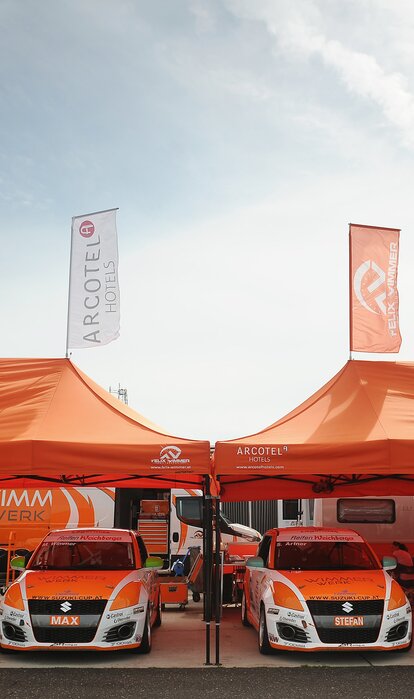  Orange 8x4 gazebo with black frame and two customised flags with Wimmer Werk logo. Paddock gazebo for rally racing cars.