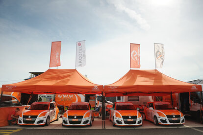 Gazebo 8x4 arancione con struttura nera e due bandiere personalizzate con logo Wimmer Werk. Gazebo paddock per auto da corsa rally.