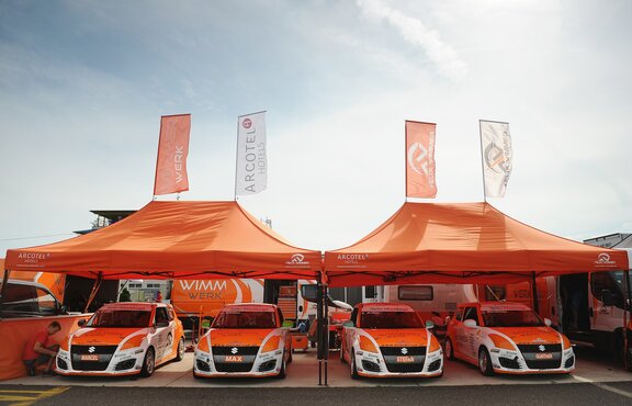 Gazebo 8x4 arancione con struttura nera e due bandiere personalizzate con logo Wimmer Werk. Gazebo paddock per auto da corsa rally.