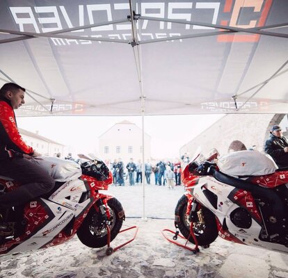 Zwei rote Motorrad-Rennfahrer stehen mit dem Motorrad unter dem Faltpavillon.