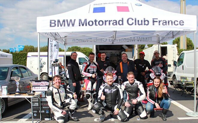 Weißes Rennzelt mit der Aufschrift "BMW Motorrad Club France". Darunter hockt das Rennteam.