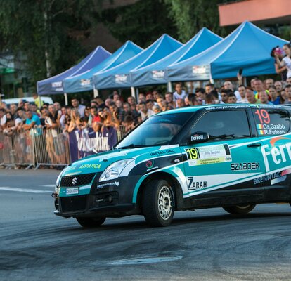 Blaue Faltpavillons neben der Rennstrecke bei einem Racingevent. Davor steht ein trükises Rennfahrzeug von Suzuki.