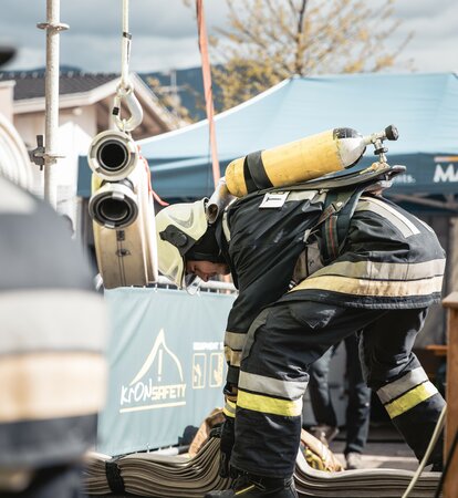 Feuerwehrmann mit Atemschutzgerät erledigt etwas am Boden. Dahinter steht ein blauer Faltpavillon mit der Aufschrift MASTERTENT.