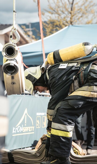 Feuerwehrmann mit Atemschutzgerät erledigt etwas am Boden. Dahinter steht ein blauer Faltpavillon mit der Aufschrift MASTERTENT.