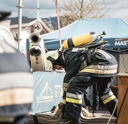 Feuerwehrmann mit Atemschutzgerät erledigt etwas am Boden. Dahinter steht ein blauer Faltpavillon mit der Aufschrift MASTERTENT.