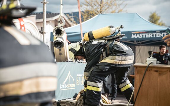 Feuerwehrmann mit Atemschutzgerät erledigt etwas am Boden. Dahinter steht ein blauer Faltpavillon mit der Aufschrift MASTERTENT.