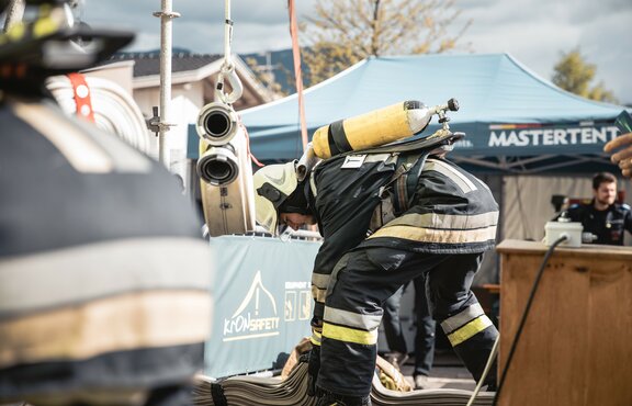 Feuerwehrmann mit Atemschutzgerät erledigt etwas am Boden. Dahinter steht ein blauer Faltpavillon mit der Aufschrift MASTERTENT.
