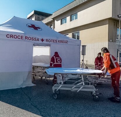 The Red Cross staff carries the corona patient to the rescue tent. The Rescue Kit tent is white. 