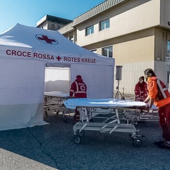 The Red Cross staff carries the corona patient to the rescue tent. The Rescue Kit tent is white. 
