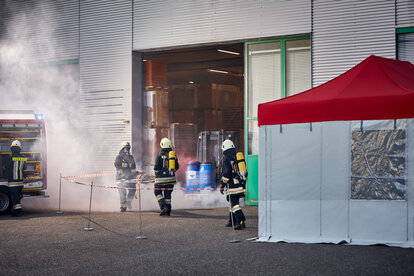 The firemen are carrying a victim of a chemical accident out of the hall. They are bringing the injured person to the gazebo. 