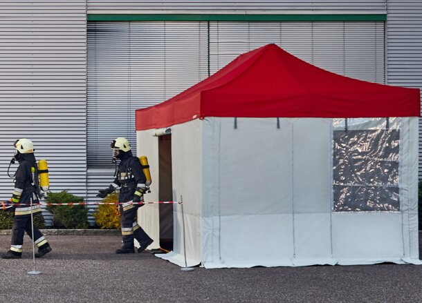Les pompiers transportent la victime dans la tente Rescue. La tente Rescue est équipée d'un toit rouge et de parois grises.