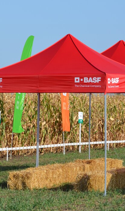 Red gazebo is standing on the field. Below it are some bales of straw. 