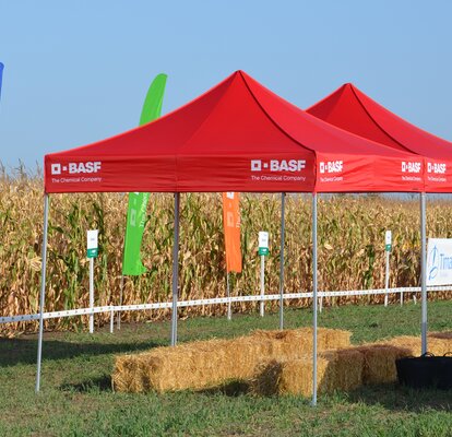 Red gazebo is standing on the field. Below it are some bales of straw. 