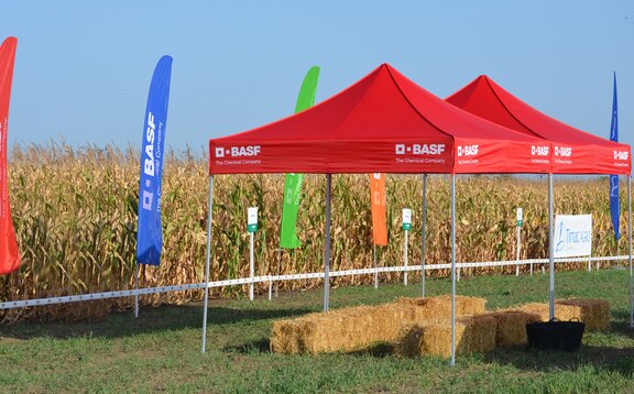Red gazebo is standing on the field. Below it are some bales of straw. 
