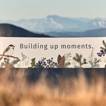 Il gazebo pieghevole bianco con tetto piatto è stampato con motivi forestali come uccelli, pigne e foglie. Sopra c'è scritto "building up moments".