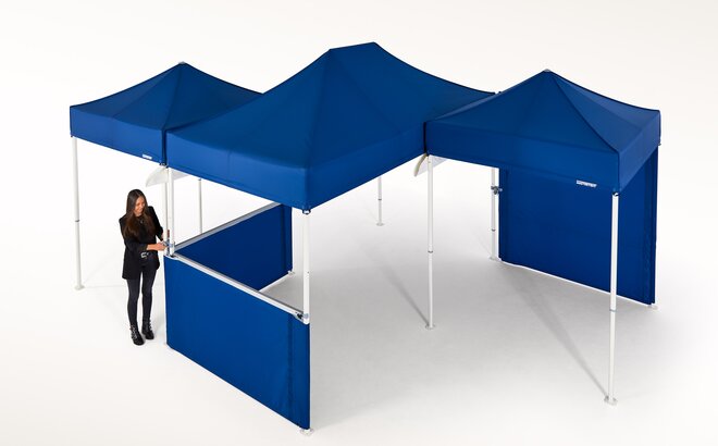 Woman is currently connecting several blue gazebos and is thereby creating a larger covered area.