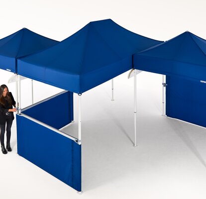 Woman is currently connecting several blue gazebos and is thereby creating a larger covered area.