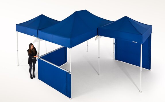 Woman is currently connecting several blue gazebos and is thereby creating a larger covered area.