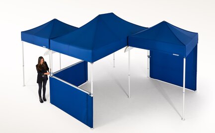 Woman is currently connecting several blue gazebos and is thereby creating a larger covered area.