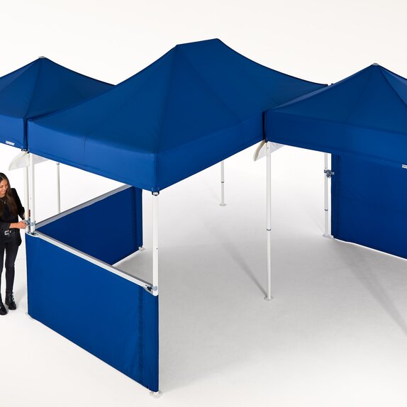 Woman is currently connecting several blue gazebos and is thereby creating a larger covered area.