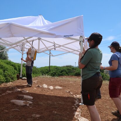Persone montano un gazebo pieghevole bianco durante gli scavi archeologici sul campo. La tenda da cantiere serve come copertura mobile e protezione dal sole quando si lavora all'aperto.