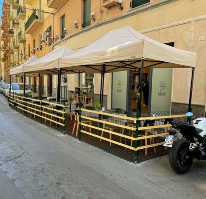 Gazebo pieghevole elegante e moderno beige 4x2 m con struttura in alluminio nera. Fila di gazebo utilizzati nell'area esterna del locale bar ristorante Maké per le vie della città