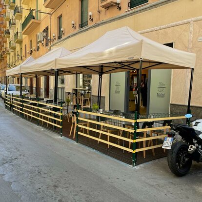 Gazebo pieghevole elegante e moderno beige 4x2 m con struttura in alluminio nera. Fila di gazebo utilizzati nell'area esterna del locale bar ristorante Maké per le vie della città