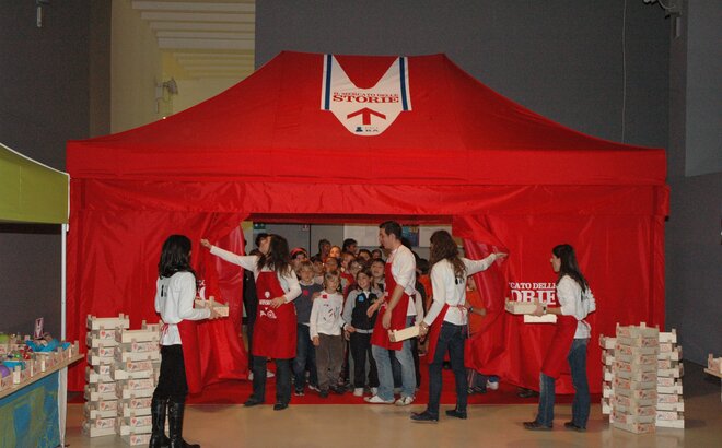 Gazebo pieghevole rosso 4x2 con pareti laterali. Il gazebo è personalizzato con logo "Il supermercato delle storie" e viene utilizzato per attività ricreative con i bambini