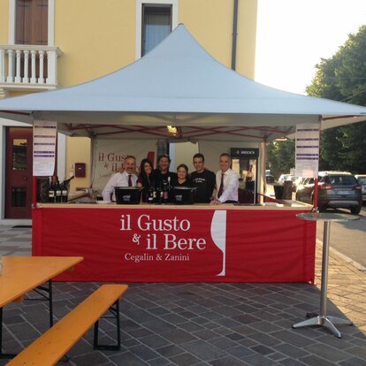 Gazebo pieghevole 4x4 m bianco con struttura rossa e pareti laterali a mezza altezza rosse con logo "il gusto del bere" e con bancone  per servizio vino a evento all'aperto. 