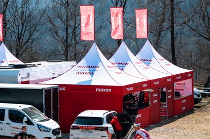 Gazebo rossi e bianchi con veli pubblicitari sono allestite all'esterno, insieme a diversi veicoli.