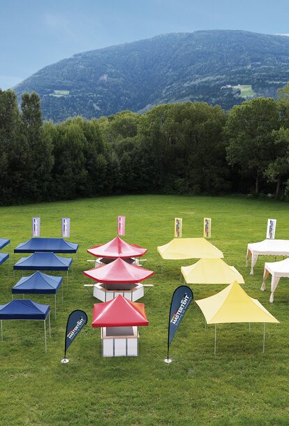 All gazebos of all sizes and designs are separated according to colour. They stand on a large field. The gazebos are either blue, red, yellow or ecru.
