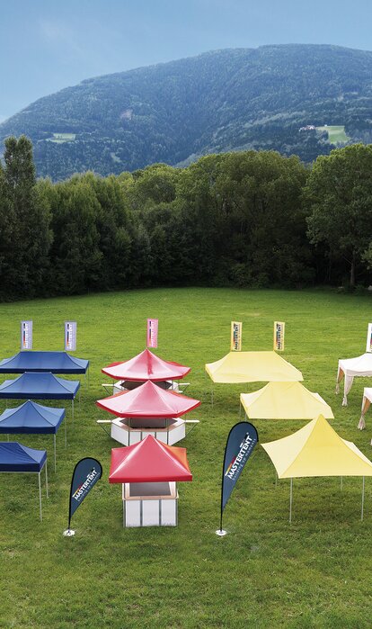 All gazebos of all sizes and designs are separated according to colour. They stand on a large field. The gazebos are either blue, red, yellow or ecru.