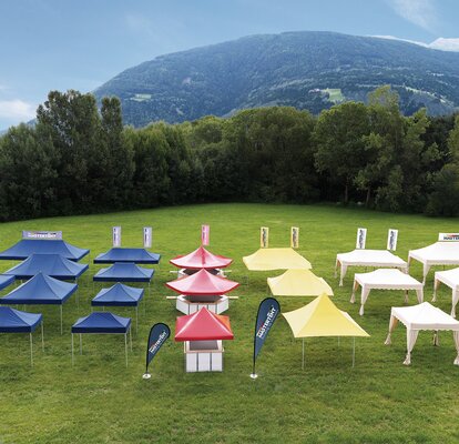 All gazebos of all sizes and designs are separated according to colour. They stand on a large field. The gazebos are either blue, red, yellow or ecru.