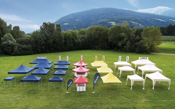 All gazebos of all sizes and designs are separated according to colour. They stand on a large field. The gazebos are either blue, red, yellow or ecru.