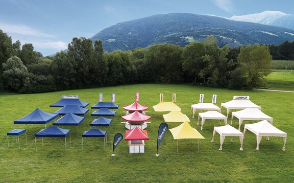 Tutti i gazebo pieghevoli di tutte le dimensioni e design sono allineati a colori su un grande prato. I gazebo pieghevoli sono blu, rossi, gialli e ecrù.