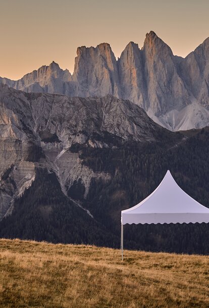 The white pagoda tent stands on the mountain. Behind it stretches a dreamlike mountain range in the sunset.