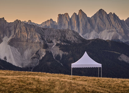 The white pagoda tent stands on the mountain. Behind it stretches a dreamlike mountain range in the sunset.