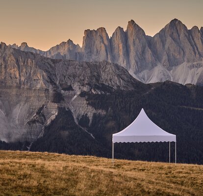 The white pagoda tent stands on the mountain. Behind it stretches a dreamlike mountain range in the sunset.