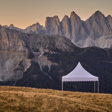 Das weiße Pagodenzelt steht am Berg. Dahinter erstreckt sich eine traumhafte Bergkette im Sonnenuntergang.