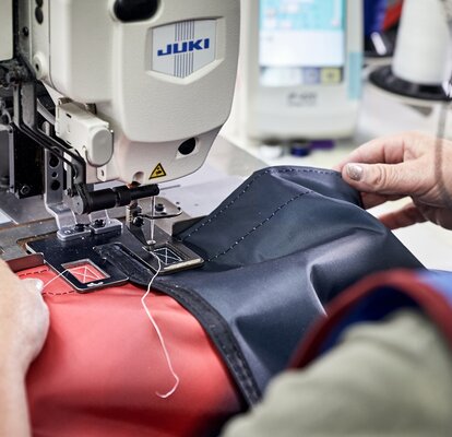 The seamstress finishes sewing the roof with the sewing machine. A blue and red fabric can be seen and a white thread.