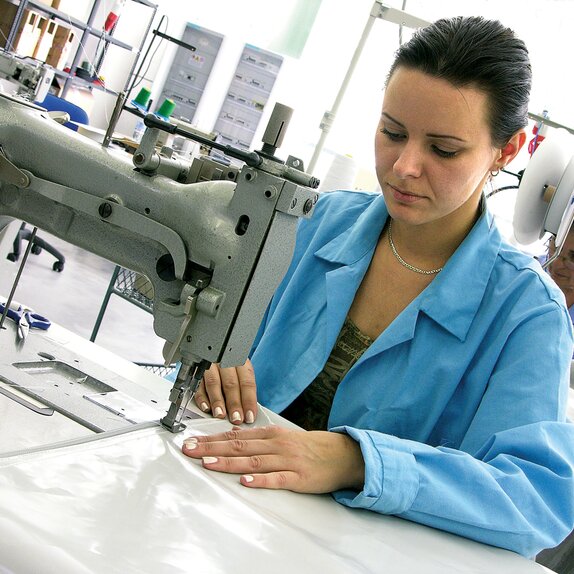 Eine Frau näht die Stoffe des Faltzeltes zusammen. Die Frau sitzt bei der Nähmaschine.