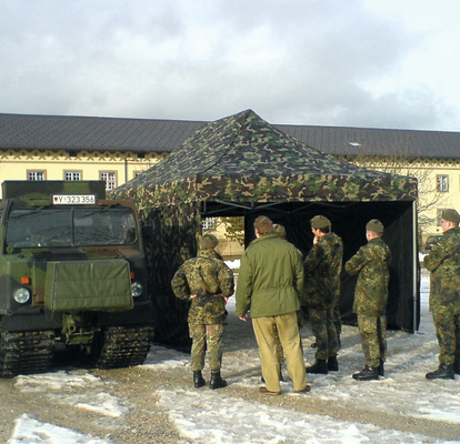 Militärzelt mit Seitenteilen auf einem verschneiten Platz vor einer Kaserne. Davor stehen mehrere Soldaten.