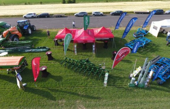 Ein Baukastensystem aus roten Faltpavillons der Firma Novaxi steht auf einer Wiese. Daneben stehen Traktoren und andere Geräte für die Landwirtschaft