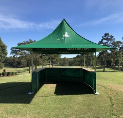 Ein grünes Faltzelt mit Theke an drei Seiten und Vordächern steht auf einem Golfplatz. 