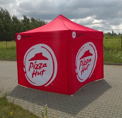 Ein rotes 3x3 m Promotionzelt steht im Freien auf einem gepflasterten Weg. Die Seitenwände sind mit dem Logo "Pizza Hut" bedruckt.