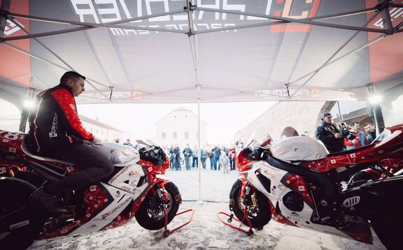 Nella tenda ci sono due motociclette, ognuna nei colori bianco, nero e rosso. Un autista é seduto sul lato sinistro di una moto.